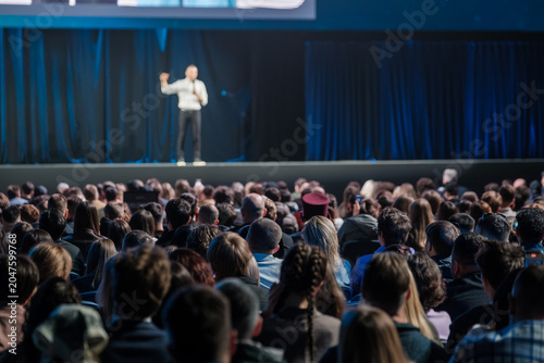 Tableau sur toile Large crowd listening to keynote speaker on stage at professional conference, moody blue lighting, focused atmosphere