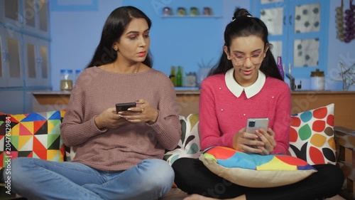Young mother and teen daughter surfing internet - modern technology. Medium shot of two females wearing woolens during winters using mobile phones - Screen time abuse and disconnected family