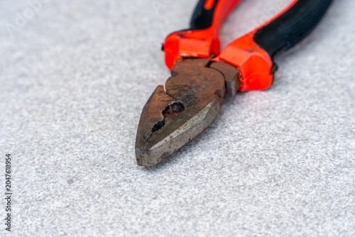 Fotografie Closeup of rusty plier jaws with red and black handle on gray background