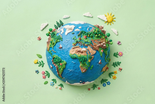 Detailed plasticine model of planet earth with sun and flowers on a light green background.