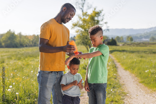 Father applies sunscreen lotion to his children while they enjoy a sunny summer day outside.