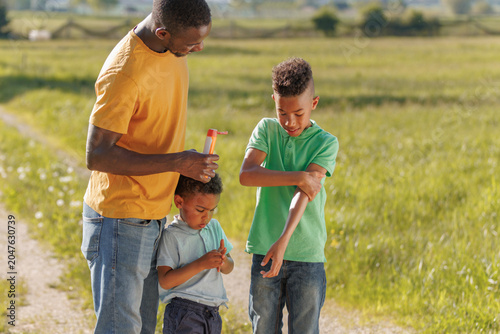 Father helps his children apply sunscreen while enjoying a sunny day outdoors in a field. They practice sun safety during family time.