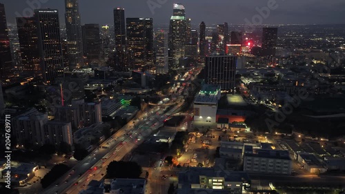Night cityscape showing downtown Los Angeles skyline, illuminated streets and heavy traffic flowing on highway with modern skyscrapers and residential buildings