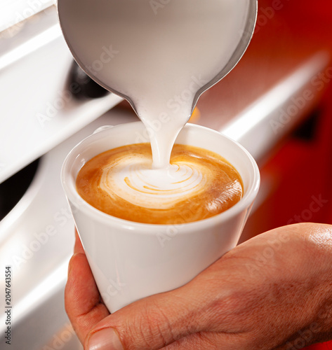 Professional barista creating a milk heart on a coffee.