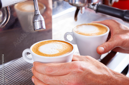 Two hands holding two cups of freshly brewed coffee.