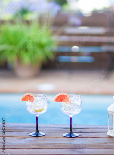 Two glasses with ice and a slice of grapefruit on a table by a pool