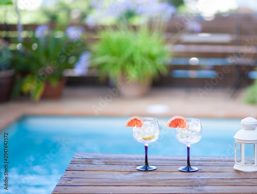 Two glasses with ice and a slice of grapefruit on a table by a pool