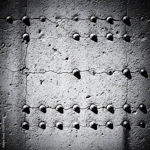 Concrete wall features a grid of protruding metal rivets set into a weathered and cracked industrial surface.