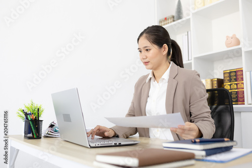 Woman types on laptop beside colorful charts. She focuses, showing professional engagement. Office setting implies analysis or presentation. Image works for business, finance, or data reporting
