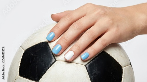 Hand holding soccer ball with blue nail polish on white background minimalist style
