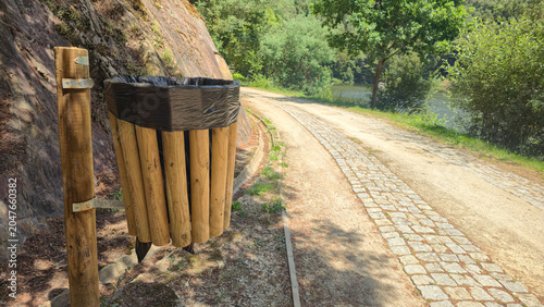 A wooden trash bin along a lakeside walkway in a green park, next to a boat. Themes: environmental responsibility, public cleanliness, sustainable recreation, and nature conservation.