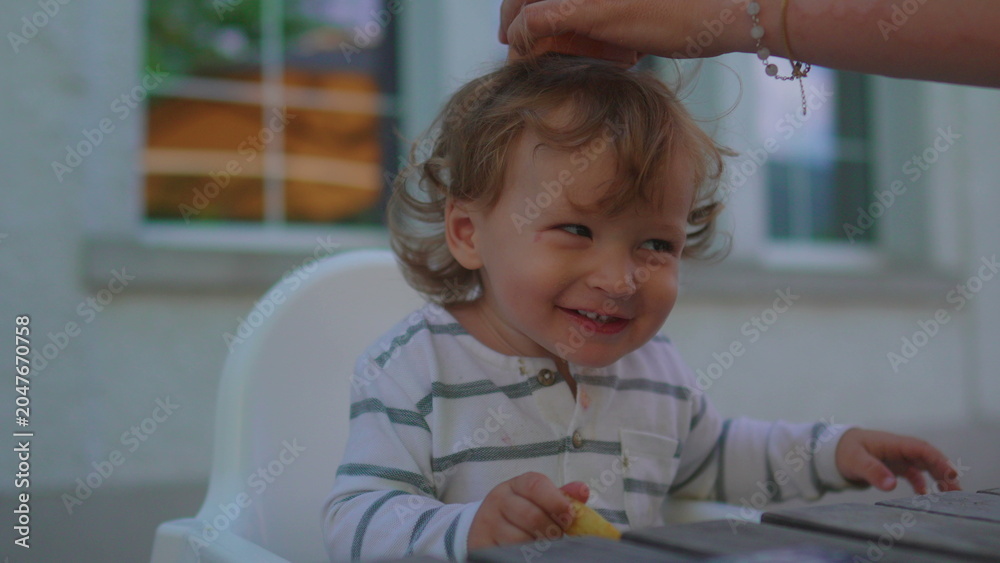 Fototapeta premium Parent balancing small cube container on toddler head during outdoor family meal capturing playful bonding, laughter and authentic parenting interaction