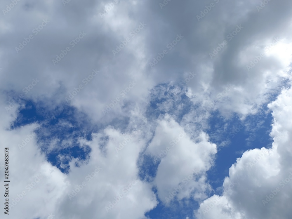 Obraz premium Dynamic sky with billowing white clouds against a blue background. Vibrant natural weather skyscape