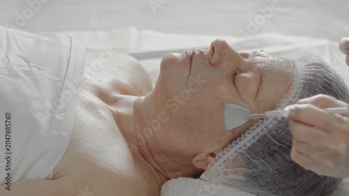 Cosmetologist does not wear an alginate mask on the face of an elderly woman in a beauty salon