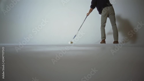 A worker paints a cyclorama in a photo studio with white paint