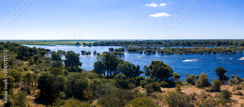 Принти на полотні Aerial panorama shows the Chobe River in Chobe National Park, Botswana, with wooded islands, riverine forest, dry savanna, floodplains, and wetlands under a clear midday sky