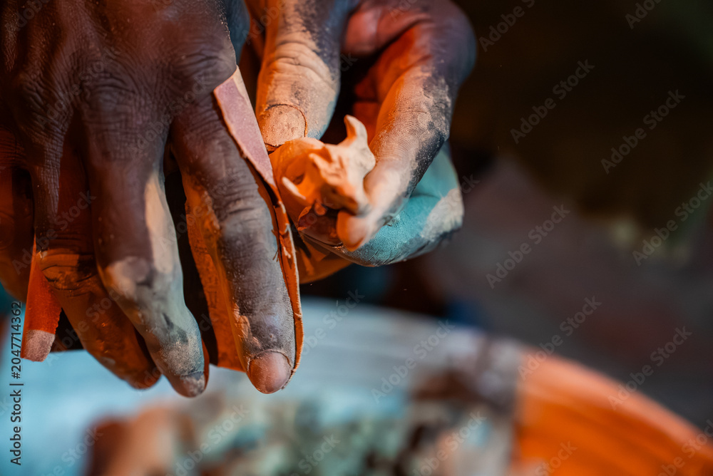 Fototapeta premium Close view of artisan hands shaping a tiny clay figurine in Zimbabwe, fingertips coated in ochre dust under warm directional light, with shallow depth of field.