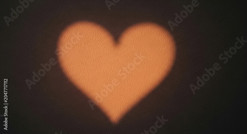 A blurred, orange heart shape on a dark background, with a soft, warm glow and a slightly textured surface.