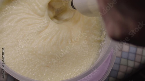 Woman's hand with mixer whipping buttercream in plastic bowl