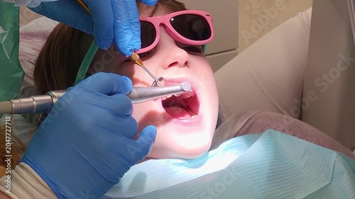 Dentist cleaning tooth of little boy wearing pink glasses. Pediatric dental care and oral health checkup in medical clinic. Professional hygiene procedure for child patient in office.