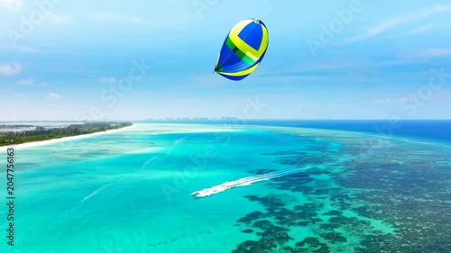 Colorful kite surfer gliding over beautiful turquoise tropical ocean water on a sunny day