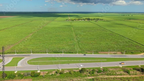 Aerial view of rural highway crossing vast green agricultural fields under sunny sky