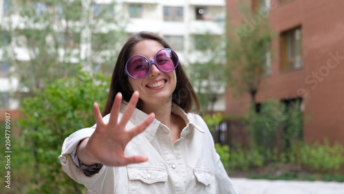 Close-up portrait of attractive young Caucasian girl smiling and looking at camera, taking selfie video. Cute woman broadcasting video with smartphone, waving at webcam