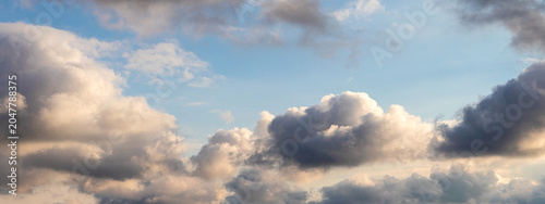 Dramatic sky with dark and light clouds on blue background in sunny evening, panoramic natural background for design