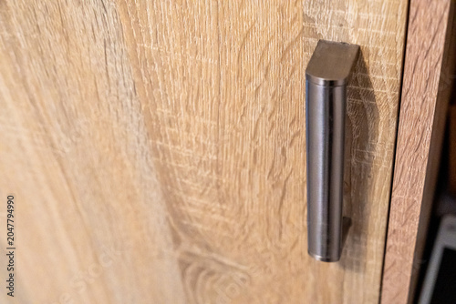 Close-up of modern cabinet wooden door with metal handle, showcasing contemporary furniture design and textures in a stylish interior setting