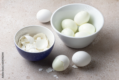 Peeled boiled eggs and eggshells in ceramic bowls on a light stone surface. Protein rich food ingredient for healthy eating, meal preparation and cooking concepts