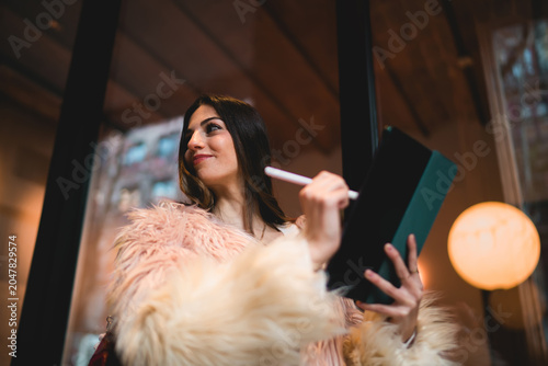 Bild auf Leinwand Happy young woman looking at camera holding stylus and tablet, successful female creator in faux fur coat enjoying creative process outdoors, authentic youth and digital lifestyle concept