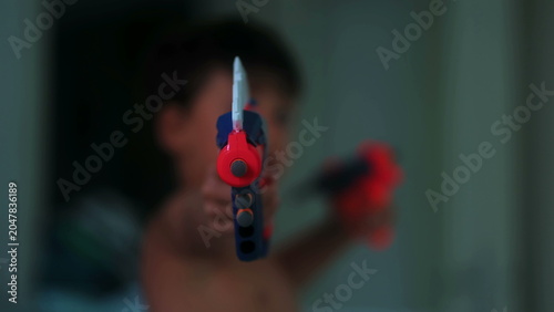 Tableau sur toile Young boy aiming colorful toy blasters toward camera during imaginative indoor p