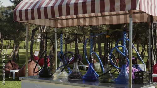 Hookahs with water stand in a row on a counter in the park with a recreation area in the background