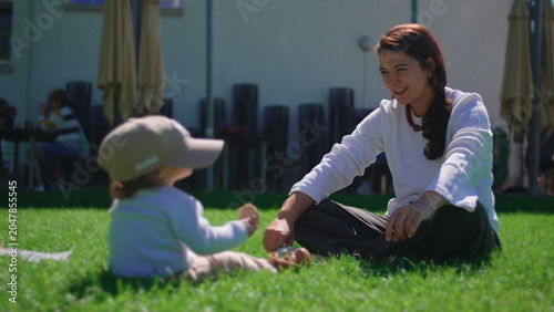 Tableau sur toile Mother smiling at toddler wearing baseball cap while sitting together on sunny g