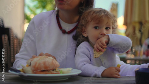 Canvas Print Toddler eating fries beside mother during outdoor family meal at sunny restauran