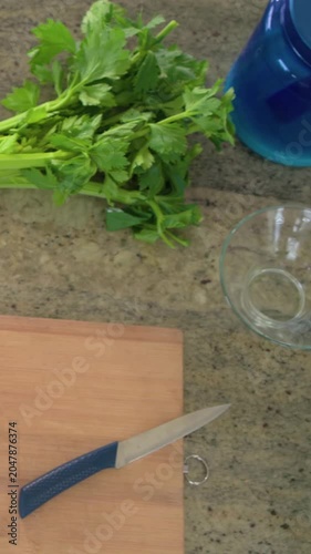 Vertical video: Shifting bunch of celery during pitcher and bowl entering on countertop, for prep