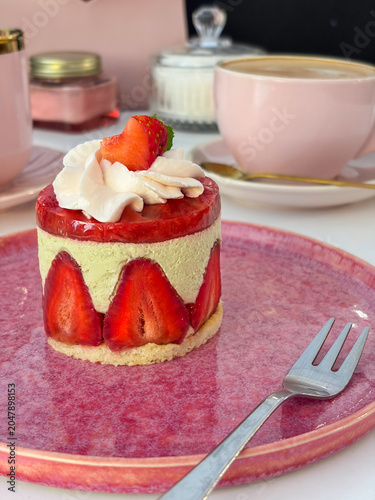Strawberry mousse cake served with fork on pink plate in cafe setting. High quality photo