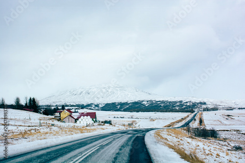 Winter asphalt road passing by rural farm houses and snow covered mountain. High quality photo