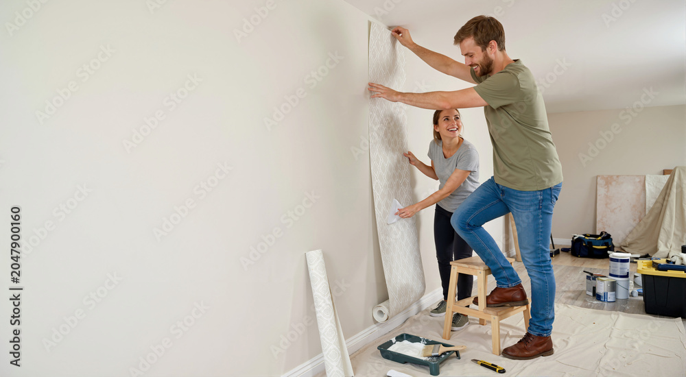Fototapeta premium Smiling couple hanging wallpaper in a room. Home renovation and DIY project