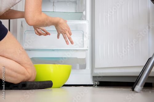 Person defrosts and cleans a freezer drawer at home, doing a household chore to maintain kitchen hygiene.