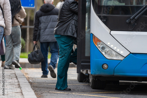 Fotografie Public transport bus picking up passengers at a designated stop, illustrating urban mobility, daily commuting, organized transit system, and passenger boarding in city environment