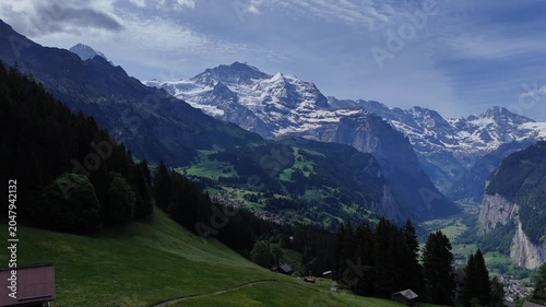 Drone landscape of the Lauterbrunnen Valley with alpine villages, forests, and snowcapped Swiss peaks under cloudy sky.