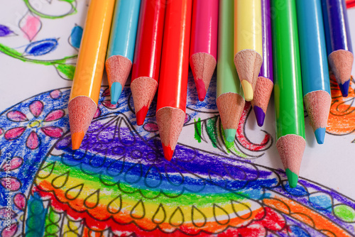 Top view macro shot of colorful wooden pencils lying on a bright hand-colored coloring book page with floral patterns