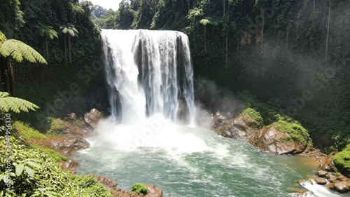 Powerful tropical waterfall cascading into a pristine pool surrounded by lush green foliage and forest