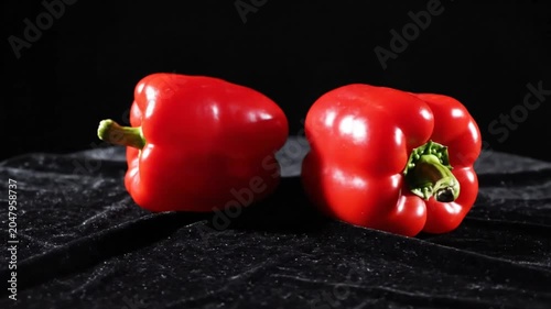 Red bell peppers on a dark textured surface against a black backdrop with dramatic lighting, studio shot