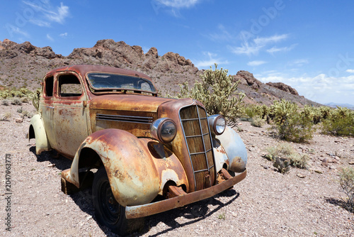 Rusty vintage car abandoned in Mojave desert under blue sky 