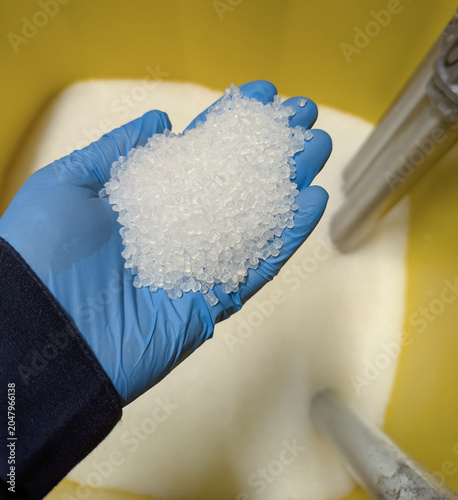 Gloved Hand Holding Clear Plastic Pellets Resin Granules in Yellow Industrial Container for Manufacturing