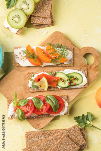Fresh crunchy rye crispbreads with different toppings on green table, top view