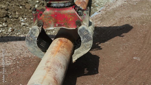Excavator Grapple Handling Large Steel Pipe at Construction Site