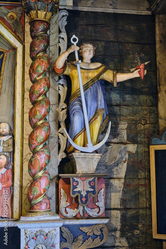 Lund, Sweden - 02 August 2025: View of an allegorical wooden statue holding an anchor and a heart inside the Kulturen open air museum with ornate painted carvings and a twisted column.
